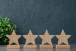 Wooden star shapes on stands arranged in a row with a green plant in the background, suggesting a theme of rating or achievement.