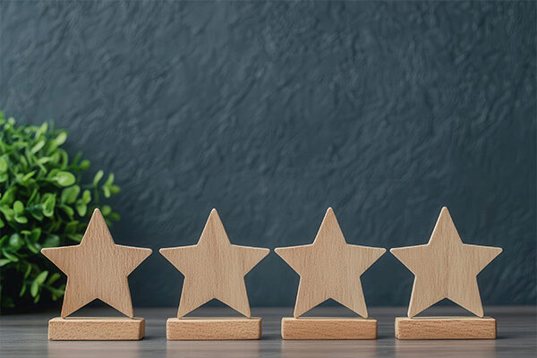 Wooden star shapes on stands arranged in a row with a green plant in the background, suggesting a theme of rating or achievement.